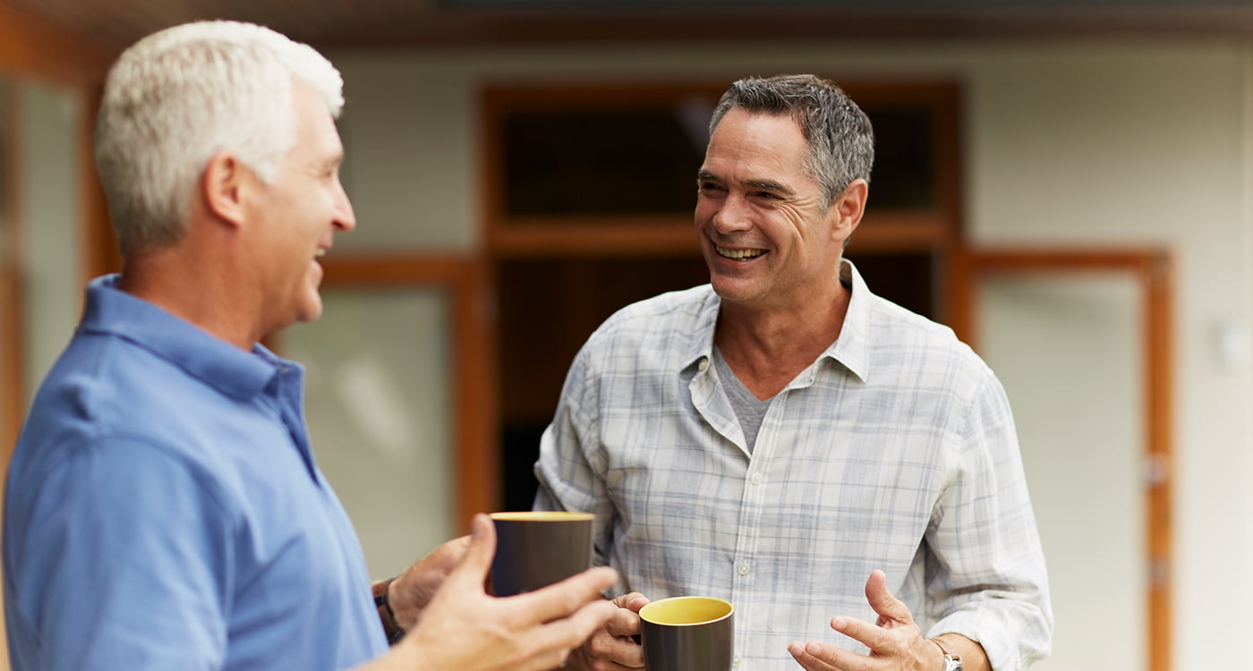 two men laughing with each other holding mugs